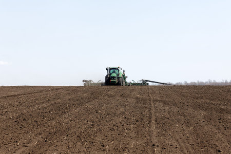 Kharkiv, Ukraine - April 10, 2019: Green tractor with trailed seeder working in field in a sunny spring day in Kharkiv Oblast, Ukraine on April 10, 2019のeditorial素材