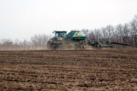 Kharkiv, Ukraine - April 10, 2019: Green tractor with trailed seeder working in field in a sunny...