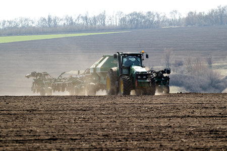 Kharkiv, Ukraine - April 10, 2019: Green tractor with trailed seeder working in field in a sunny...
