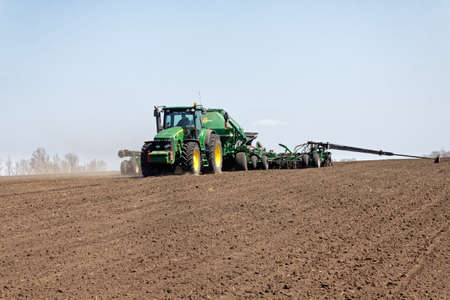 Kharkiv, Ukraine - April 10, 2019: Green tractor with trailed seeder working in field in a sunny spring day in Kharkiv Oblast, Ukraine on April 10, 2019のeditorial素材