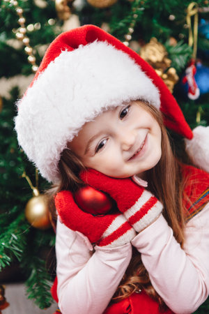 Smile girl in red hat hold a tree decoration with tree on backgroundの写真素材