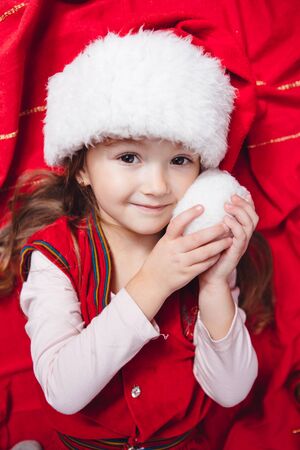 Cute girl in christmas hat on red background with decorationの写真素材