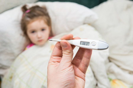 Sick little girl holding thermometer laying in bed with grumpy faceの写真素材