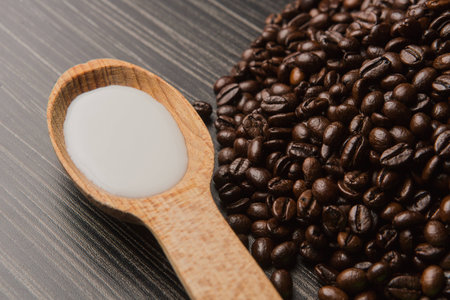 Coffee beans with milk in wooden spoon on dark backgroundの写真素材