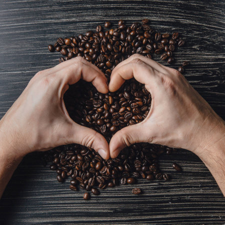 Male hands holding coffee beans in shape of heartの写真素材