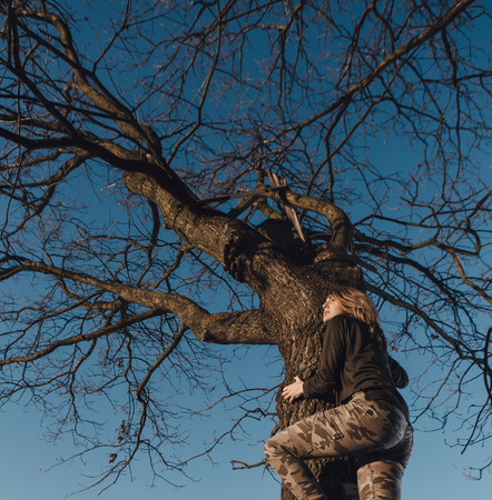 Young girl on a tree on sunset on sky backgroundの写真素材