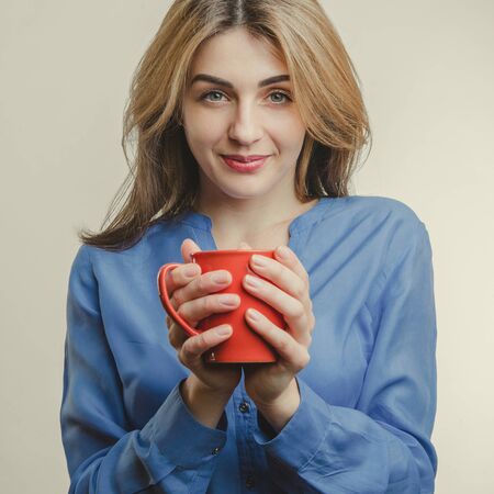 Beautiful lady in blue shirt drinks tea on white backgroundの写真素材