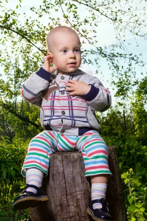 Baby boy (1 year) sitting on a tree stump.の写真素材