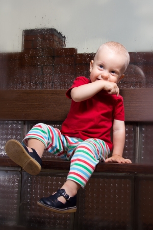 Baby boy (1 year) sitting on the bench, near the window.の写真素材