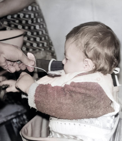 Vintage portrait of a cute little girl being fed porridge with a spoon. Retro photo from 1995.の写真素材