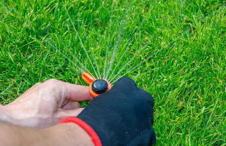 A gardener's gloved hand adjusts a sprinkler to water lawn, keeping the grass in good condition.