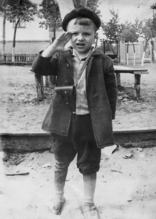 Vintage portrait of a six-year-old boy wearing a beret and a holster over his shoulder, saluting....