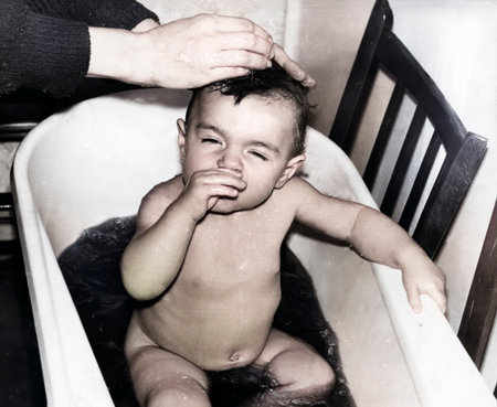 A vintage portrait of a little girl bathing in a basin. The girl is bathed in a decoction of medicinal herbs, such as string and chamomile. Retro photo from 1995.の写真素材