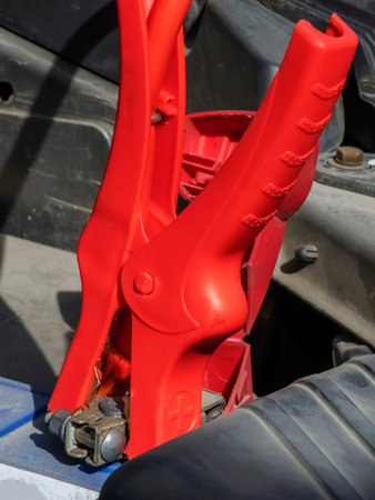 Close-up of a car charger cable jump starting a dead car battery. Red charging cable clamps on battery terminals for charging, car repair and maintenance concept.の写真素材