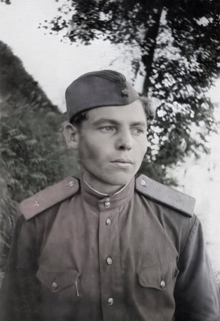 A vintage portrait of a young Soviet Army soldier wearing a cap. Retro photo from 1955.