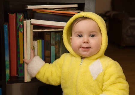 Cute baby girl in yellow dress and bookcaseの写真素材