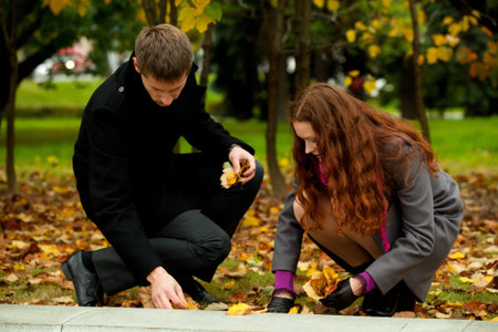 young couple in autumn park collecting leaves from trees