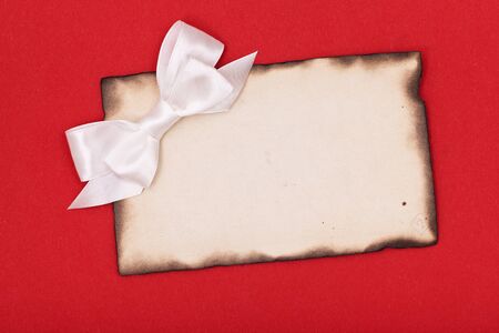 blank old burnt paper and white bow on red backgroundの写真素材