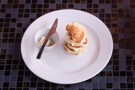 Pancakes with butter on dish with knife. Top view on tableの写真素材