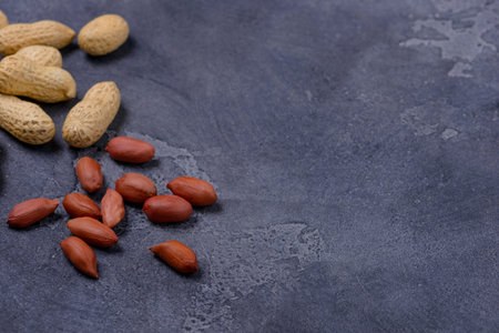 Scattered peanuts on dark stone background. Copy space for text