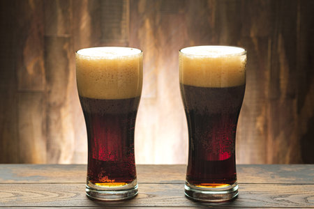 Two full glass with dark beer and foam on wooden background