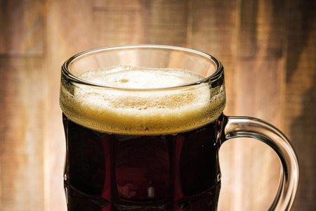 Close-up dark beer with foam in glass on wooden background
