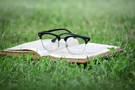 book on the grass in the park, glasses, close-up, the concept of summer vacation, reading literature in nature, rest and studyの写真素材