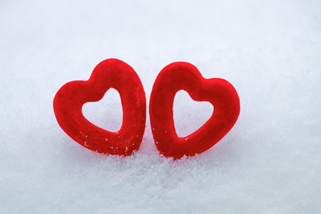 two red hearts on white snow, winter background for valentine's day, snow texture, love and happiness conceptの写真素材