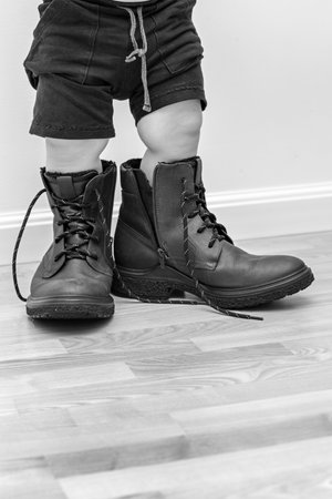 son tries on daddy's big boots, little kids feet in big shoes, big shoes, dad's day cardの写真素材