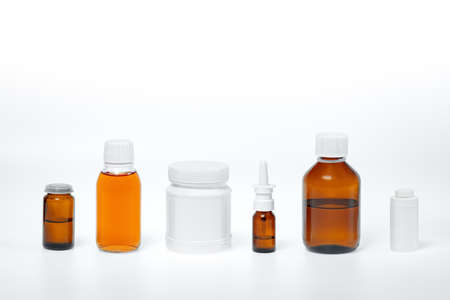 glass jars and white plastic medical containers on a white background, medicines in syrup, tinctures, drops and sprays, different forms of medicinal productsの写真素材