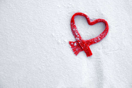 red knitted scarf in the shape of a heart on white fluffy snow, love winter, background February 14の写真素材