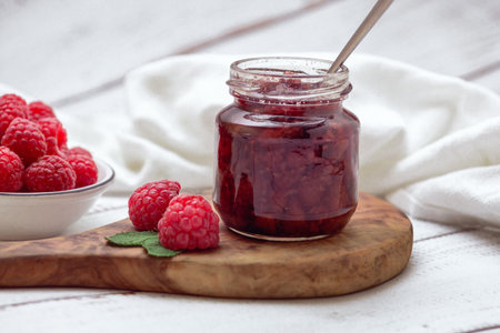 Homemade berry jam. Jar of raspberry jam and a bowl of fresh berries on a white wooden table.