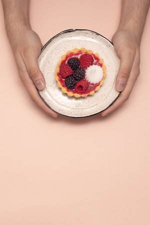 berry pie on a plate, on a beige background, hands holding a plate with fruit tart, free space for textの写真素材