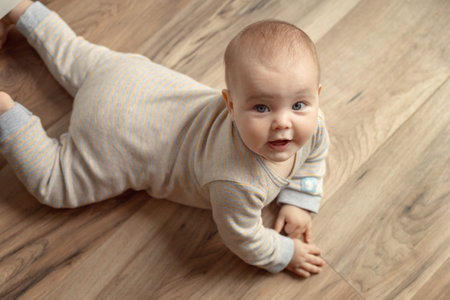 Tummy and crawling time portrait of a cute cheerful Caucasian child on the floor in a nurseryの写真素材