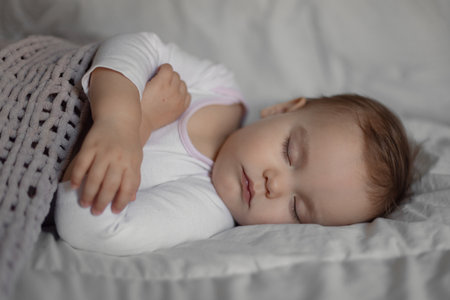 baby girl sleeps on her side in a crib on white linen, baby's daily routine, daytime sleepの写真素材