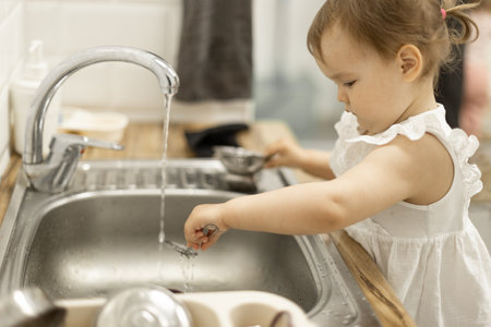 little girl 18-24 months old washes baby dishes in the sink, mother's helper,の写真素材