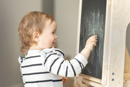 Cute little girl drawing on blackboard in kindergartenの写真素材