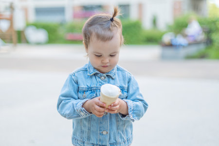 portrait of a little girl with ice cream in her hands, child eats ice cream on a hot day in park. Ice cream in a waffle cone. A happy and contented child at summer.の写真素材