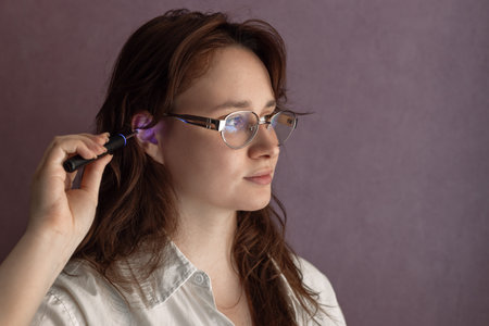 Caucasian Woman Uses Ear Wax Removal Stick, digital ear cleaner to see the inside of the ear while cleaningの写真素材