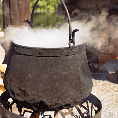 Food cooked in old cast iron outside, cauldron on open fire. Cooking on campfire in wild campingの写真素材