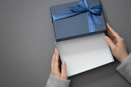 open blue empty gift box in female hands on gray background, mockup for design, free space for your productsの写真素材