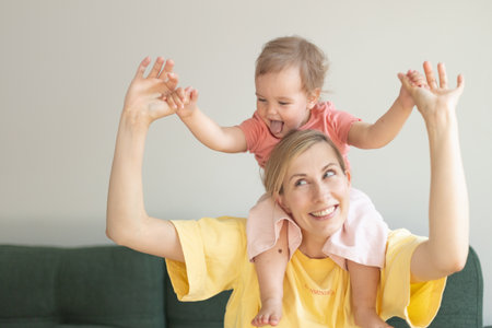 young babysitter plays with child, Kid girl play with baby sitter in living room hug her from behind laughing having funの写真素材