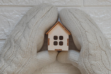 House insulation concept with hands wearing woolen mittens holding a wooden model of house.の写真素材