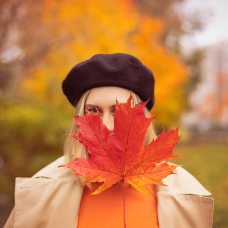 Girl holding red maple leaf in hand in colorful autumn park. Gold cozy autumn concept, warm autumn weatherの写真素材