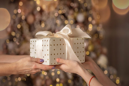 Close-up view of hands of woman giving gift box tied to bow. Giving gifts during the Christmas eve...
