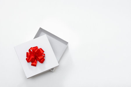 Open white gift box with a red bow on a white background, top view, free spaceの写真素材