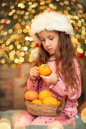 Little girl with oranges near the New Year tree, Christmas cozy mood, Christmas Eve backgroundの写真素材