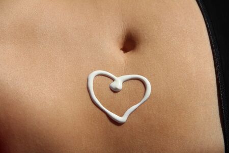 Heart of cream on tanned woman's stomachの写真素材