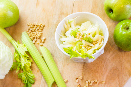 Salad with fresh cabbage, celery, apples and pine nuts, drizzled with olive oil in a salad bowl on a cutting board among the vegetables and herbs .の写真素材
