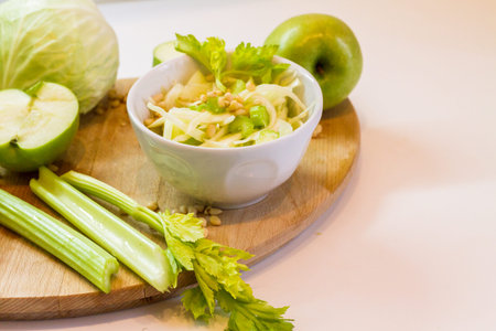 Salad with fresh cabbage, celery, apples and pine nuts, drizzled with olive oil in a salad bowl on a cutting board among the vegetables and herbsの写真素材